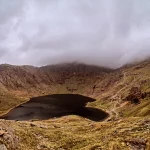 Misty snowdon surrounding a dark lake.